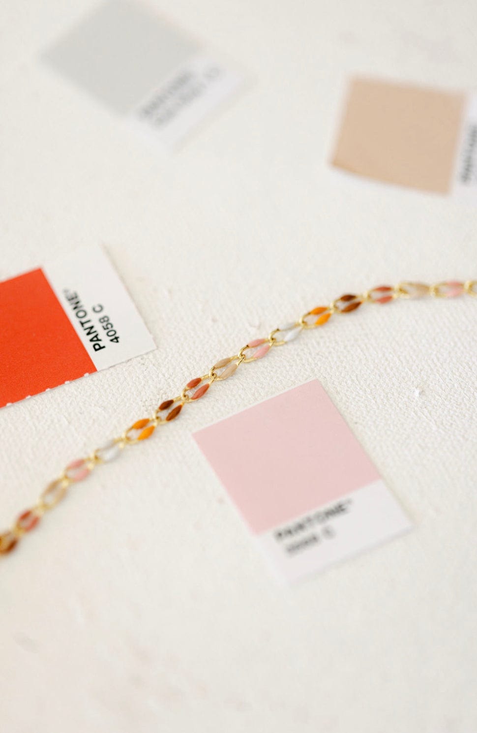 Gold chain bracelet with colorful stones and Pantone color swatches.