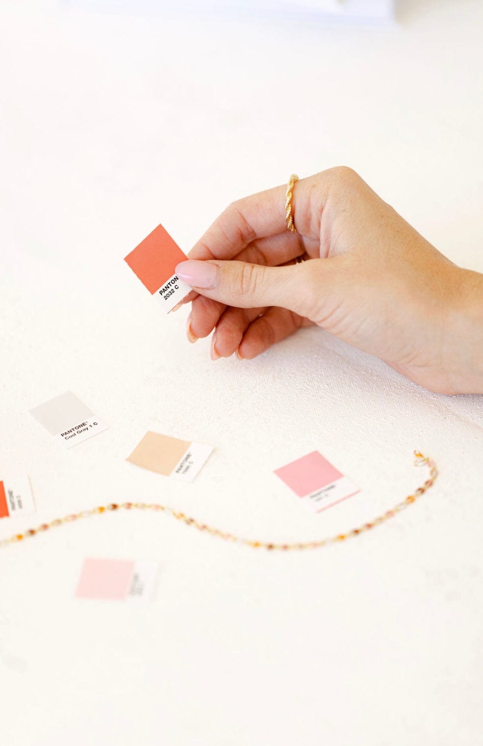 Hand holding a coral color swatch, other swatches and a gold chain.