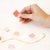 Hand holding a coral color swatch, other swatches and a gold chain.