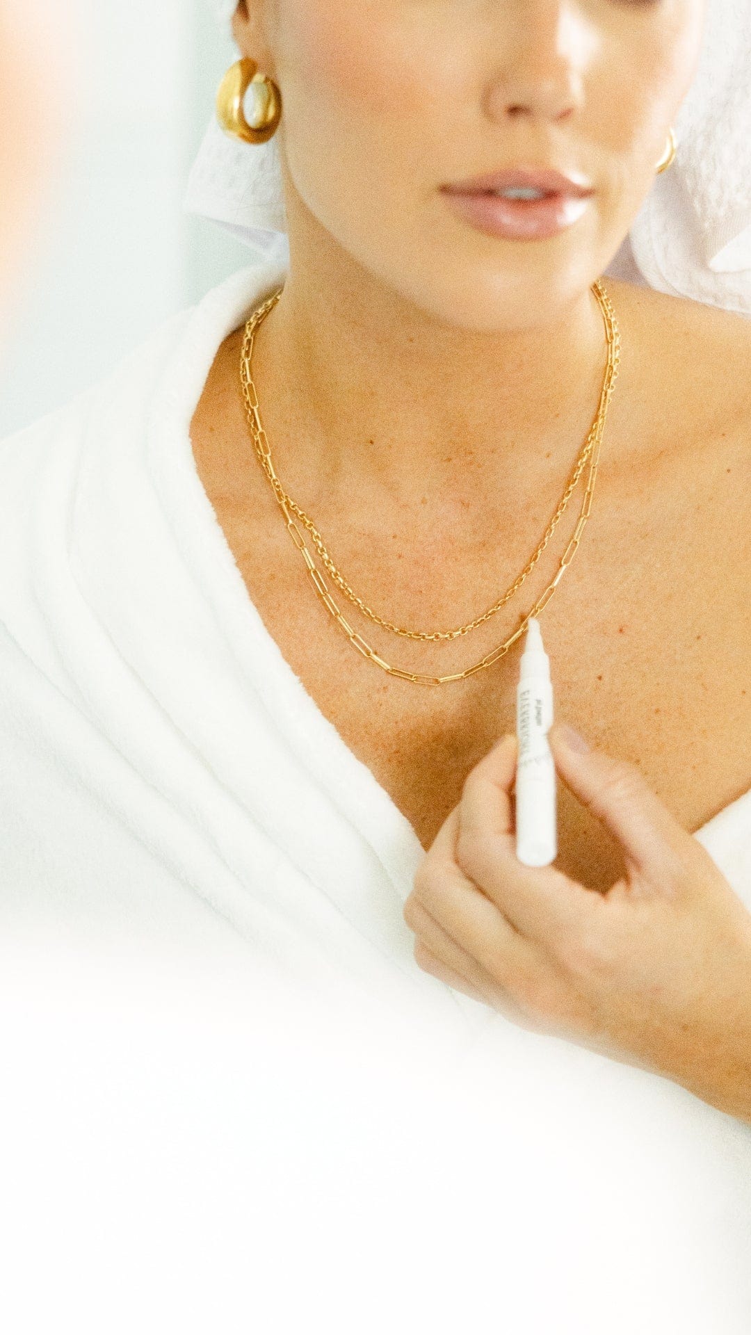 Woman in robe with jewelry holding a small tube.