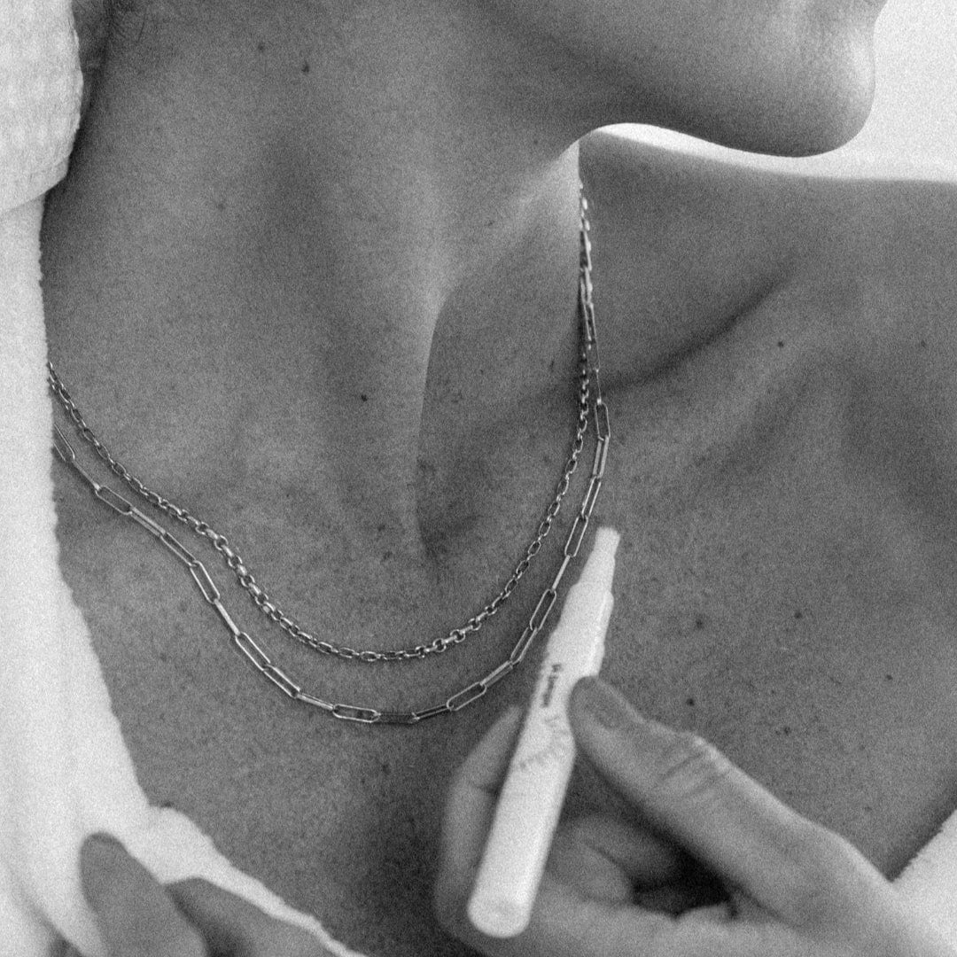 Woman in robe with necklace and skincare product.