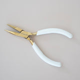 Pair of pliers with white handles and gold tips on a beige background