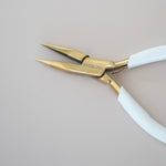 Pair of gold-handled pliers with white handles on a light gray background