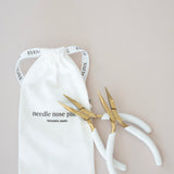 Pair of gold pliers on a white drawstring bag with text on a beige background