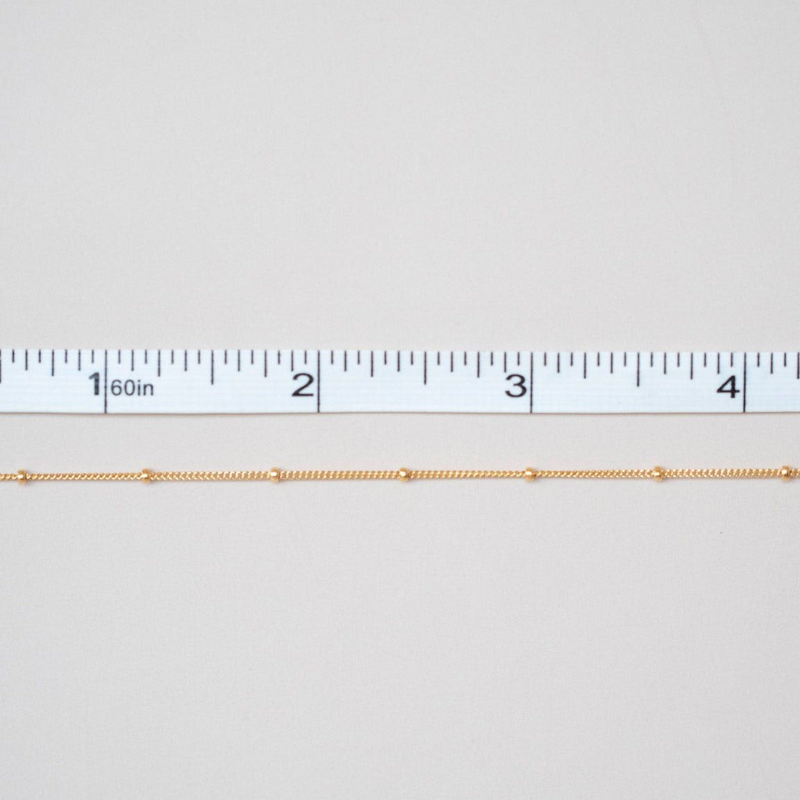 Gold chain next to a ruler on a white background