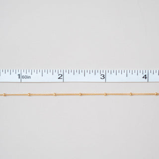 Gold chain next to a ruler on a white background