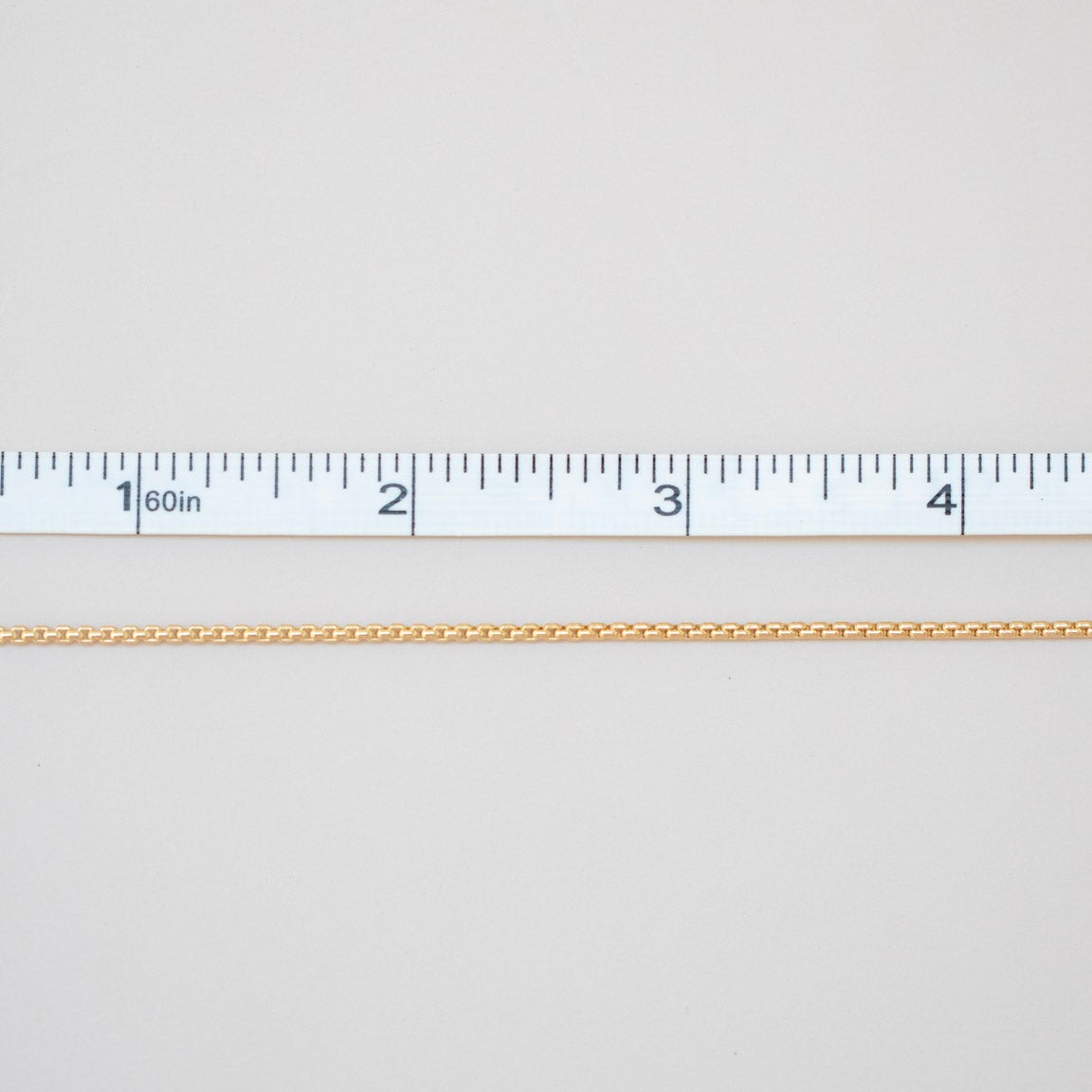 Gold chain with a ruler for scale on a light gray background