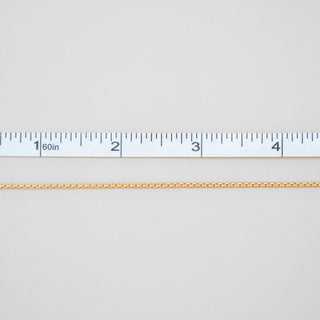 Gold chain with a ruler for scale on a light gray background