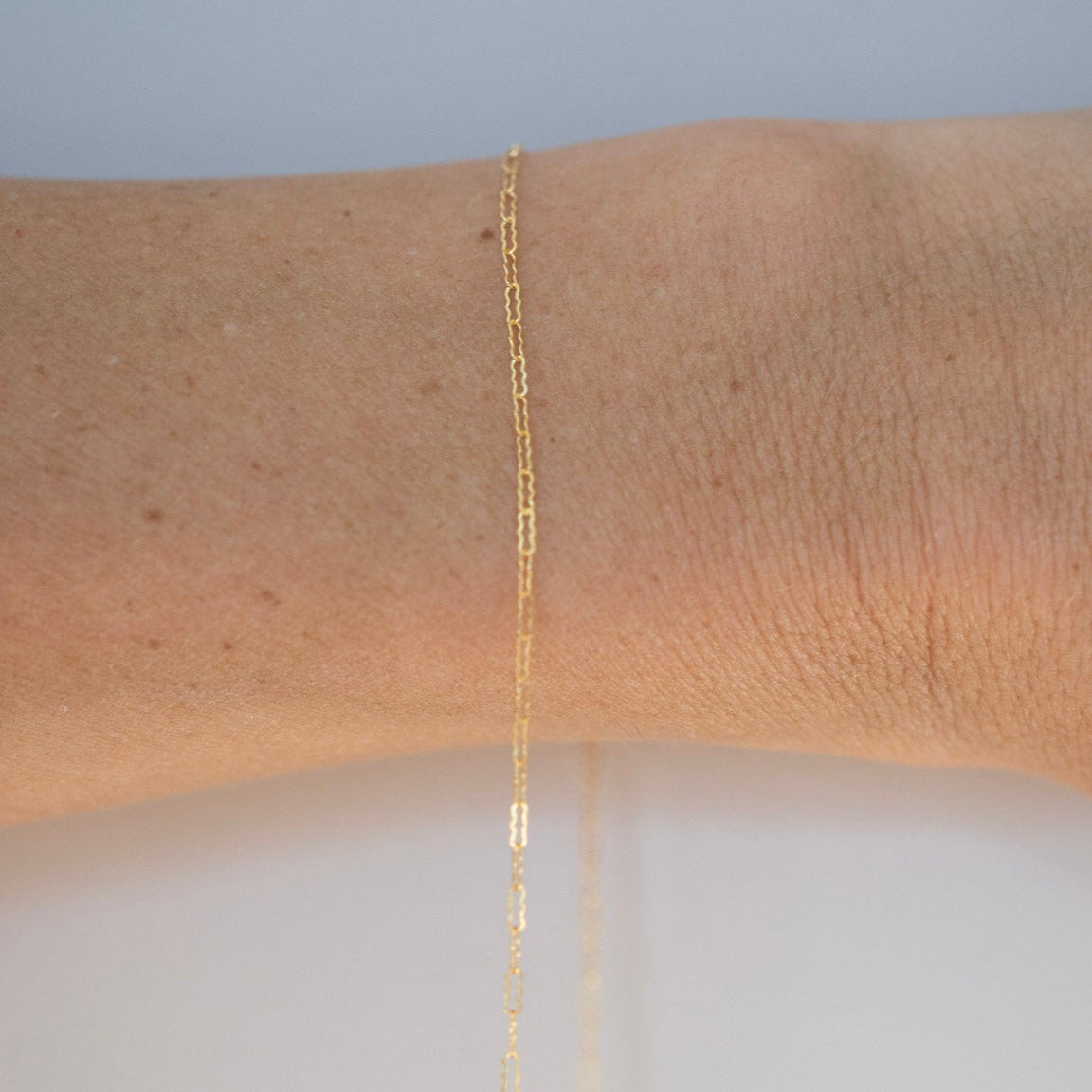 Gold bracelet on a wrist with a plain background