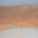 Gold bracelet on a wrist with a plain background