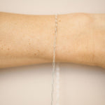Silver chain necklace on a person's arm against a beige background