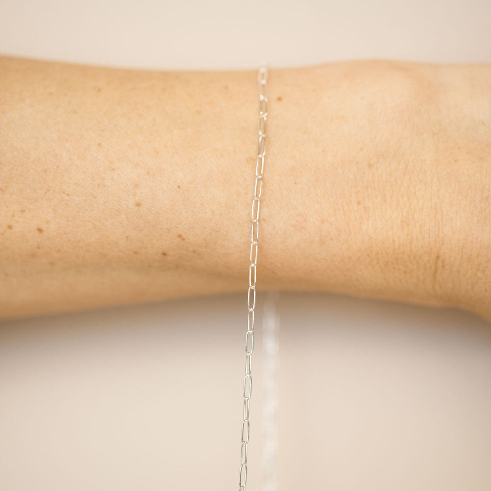 Silver chain necklace on a person's arm against a beige background
