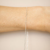 Silver chain necklace on a person's arm against a beige background
