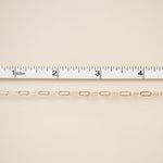 Gold chain with a ruler for scale on a beige background