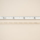 Gold chain with a ruler for scale on a beige background
