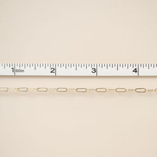 Gold chain with a ruler for scale on a beige background