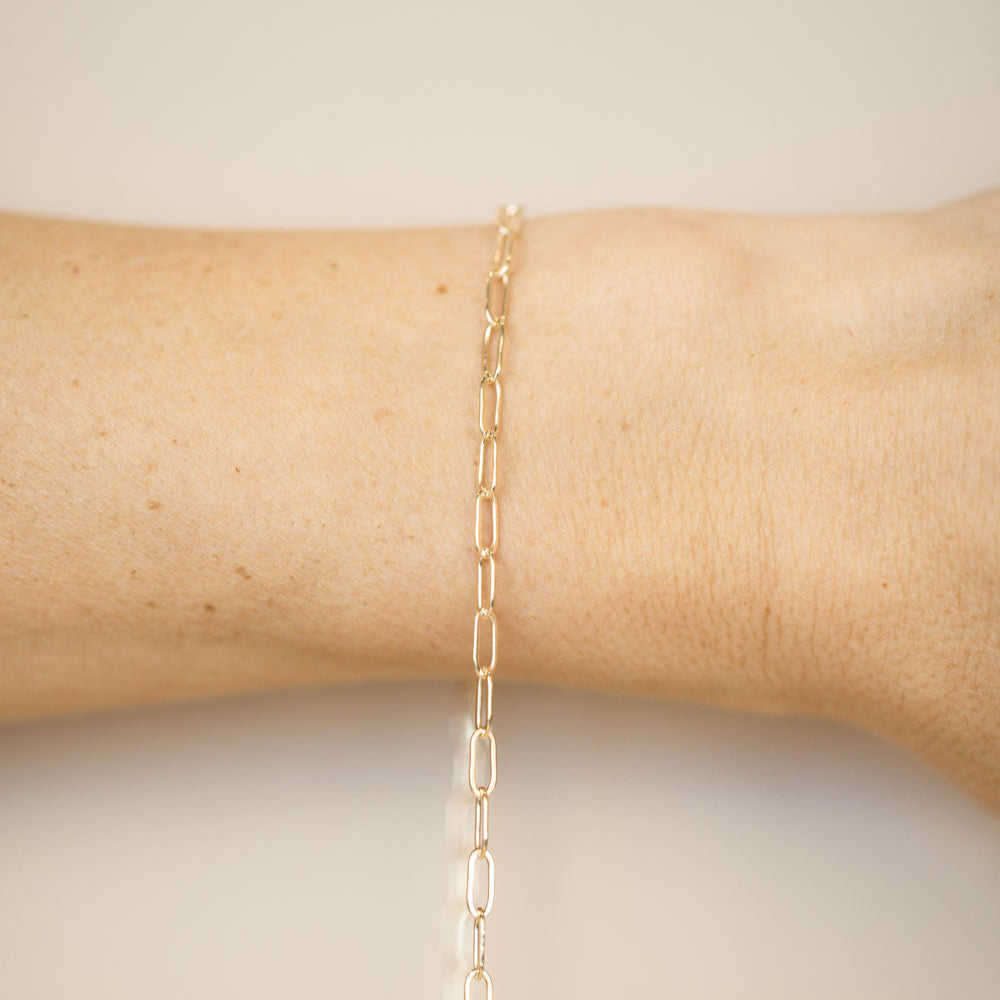 Gold chain bracelet on a wrist against a neutral background
