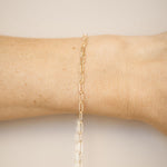 Gold chain bracelet on a wrist against a neutral background