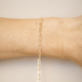 Gold chain bracelet on a wrist against a neutral background
