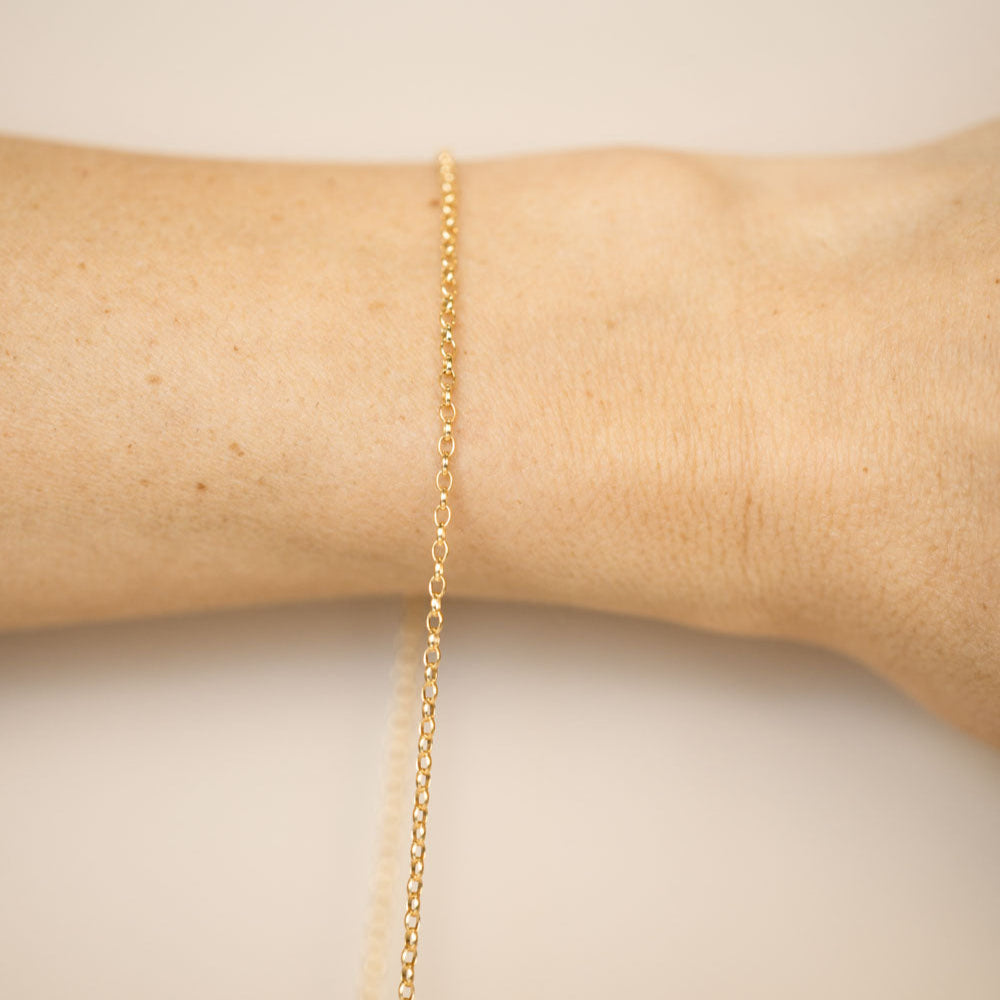 Gold bracelet on a person's wrist against a neutral background
