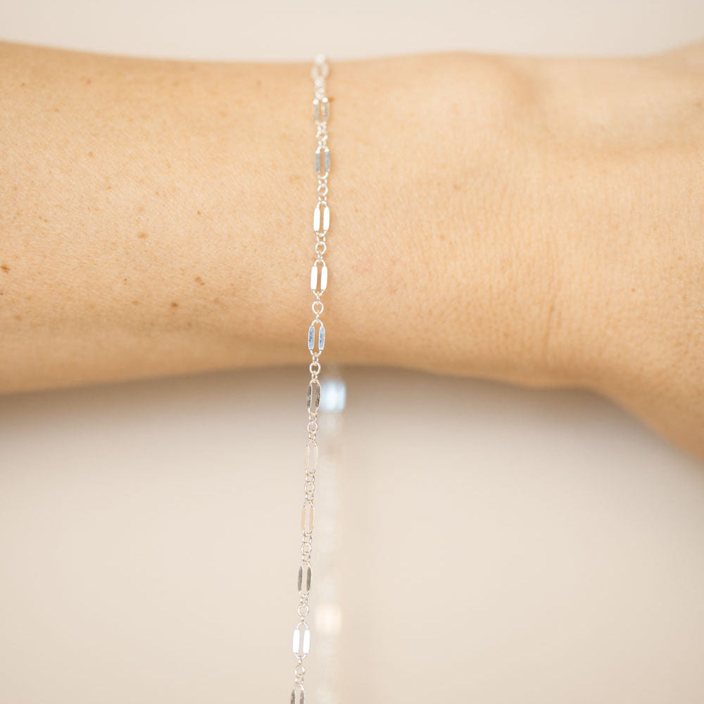 Silver chain bracelet on a wrist against a beige background