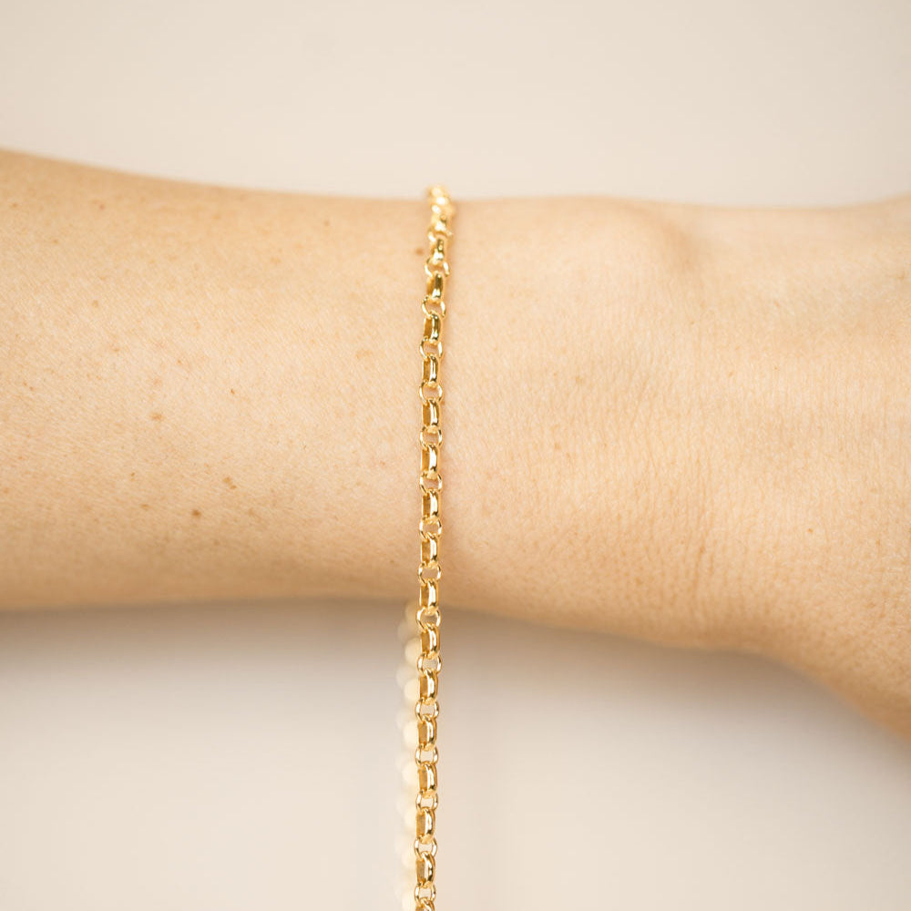 Gold bracelet on a wrist against a beige background