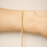 Gold bracelet on a wrist against a beige background
