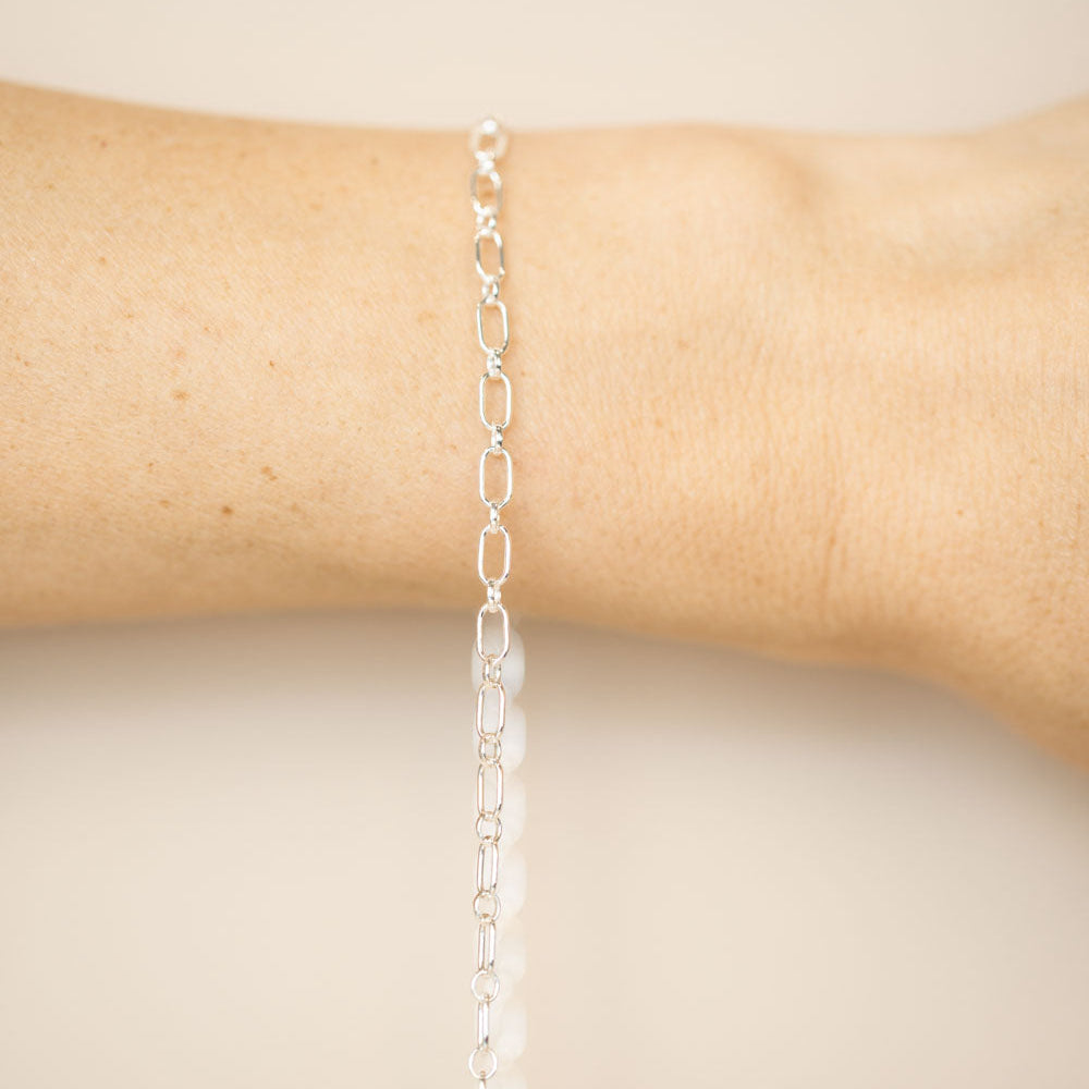 Silver chain bracelet on a wrist against a beige background