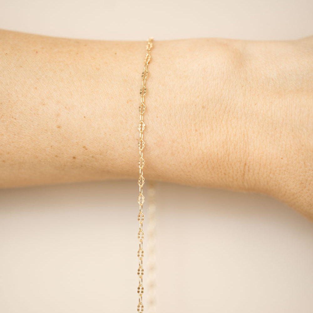 Gold bracelet on a person's wrist against a beige background