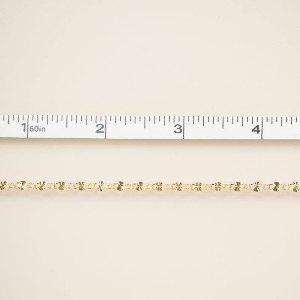 Gold chain on a beige fabric background with a ruler for scale.
