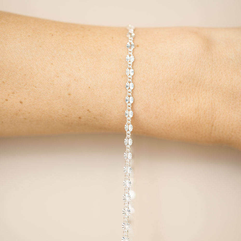 Silver bracelet on a person's wrist against a beige background