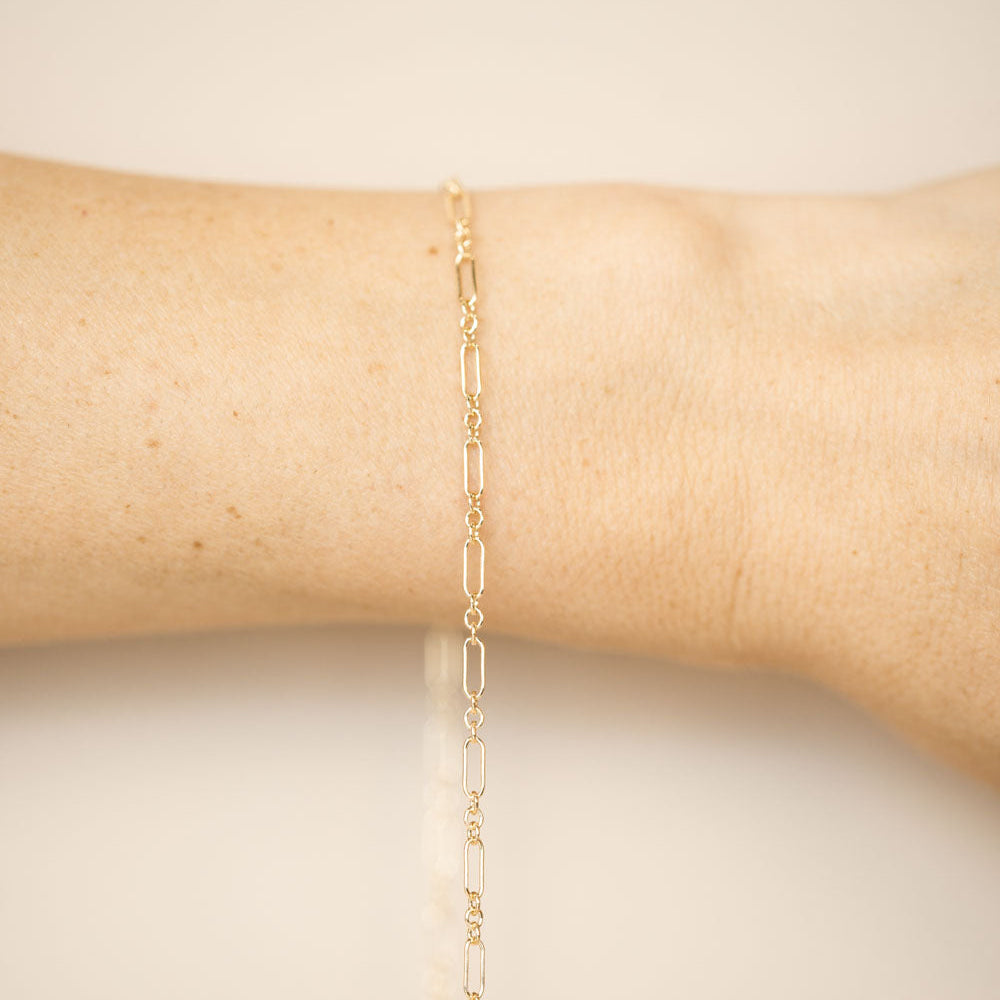 Gold chain bracelet on a person's wrist against a neutral background