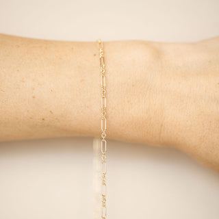 Gold chain bracelet on a person's wrist against a neutral background