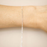 Silver chain bracelet on a person's wrist against a beige background