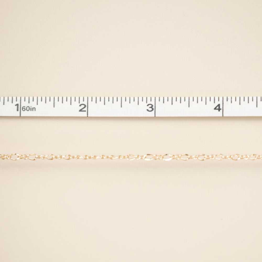 Gold chain on a beige fabric background with a ruler at the top.