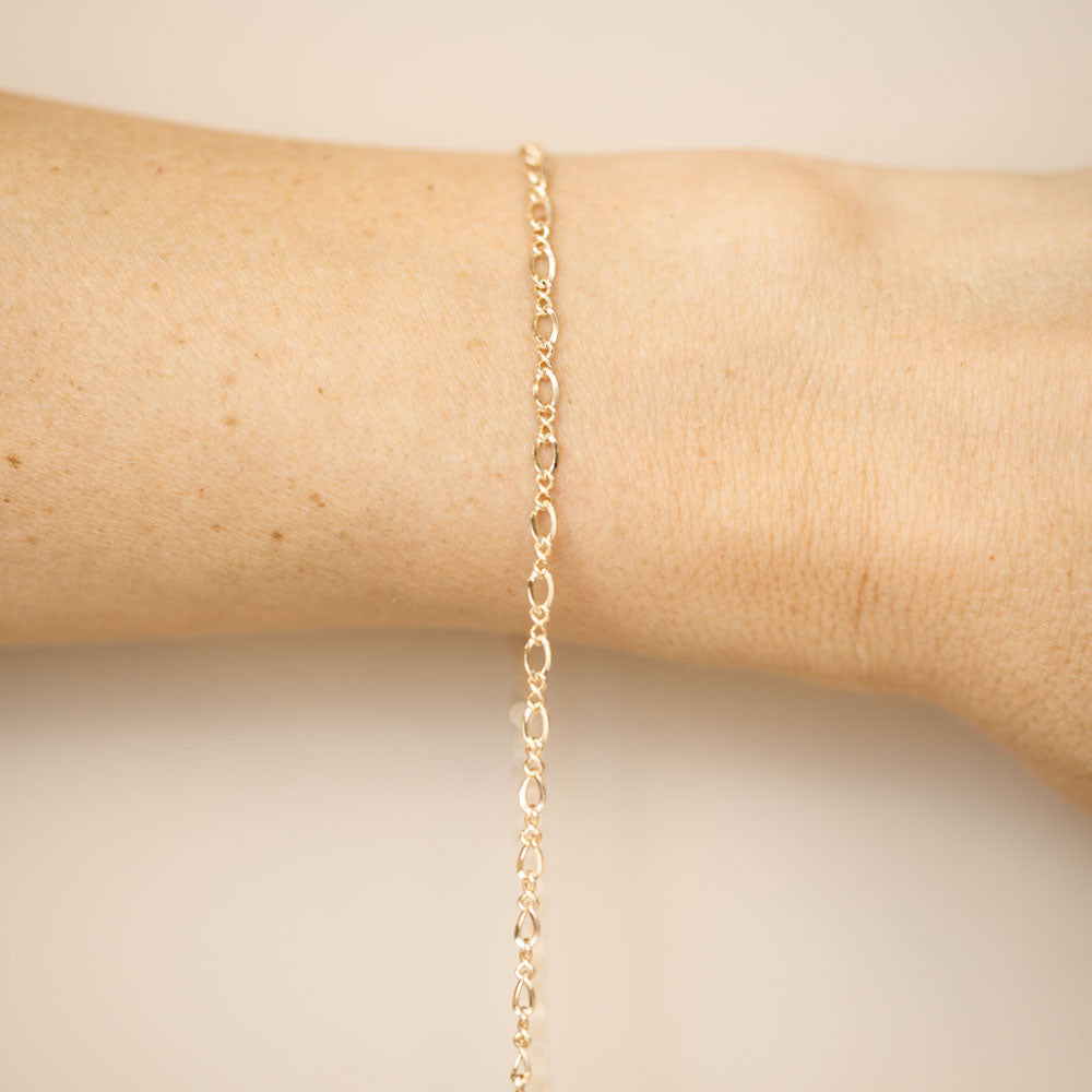 Gold chain bracelet on a wrist against a beige background