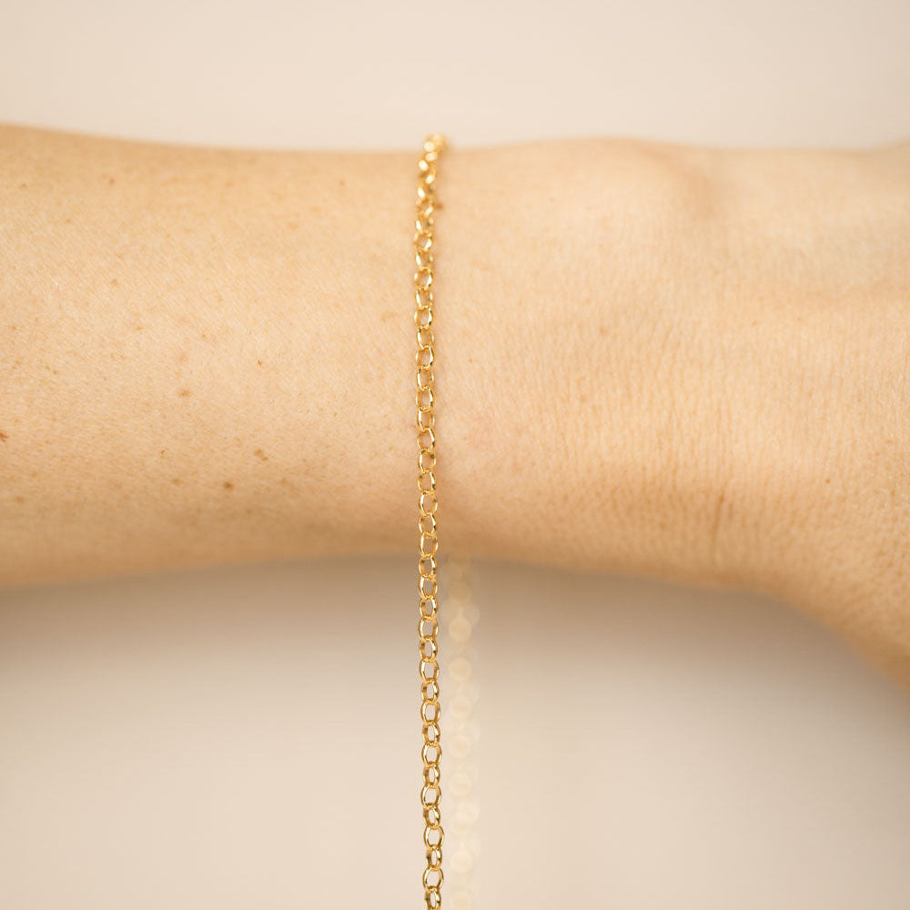 Gold chain bracelet on a person's wrist against a beige background