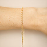 Gold chain bracelet on a person's wrist against a beige background