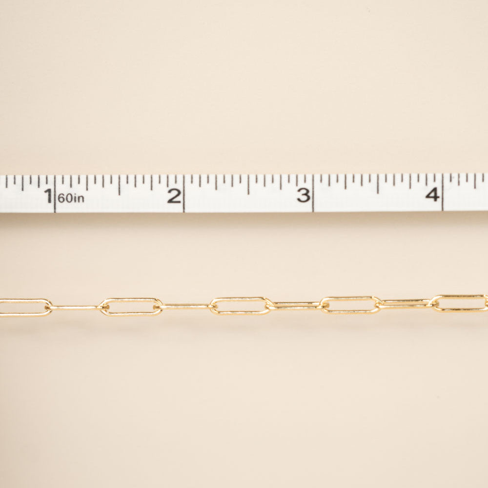 Gold chain with a ruler for scale on a beige background