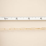 Gold chain with a ruler for scale on a beige background