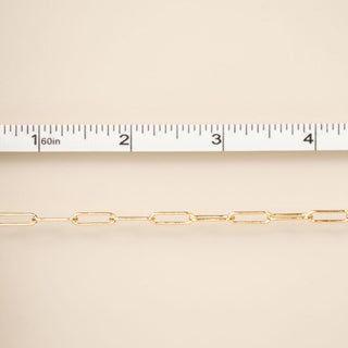 Gold chain with a ruler for scale on a beige background