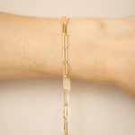Gold chain bracelet on a wrist against a beige background
