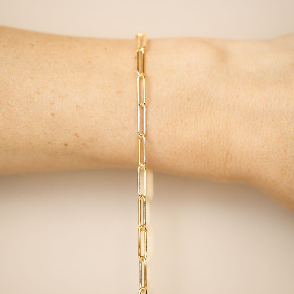 Gold chain bracelet on a wrist against a beige background