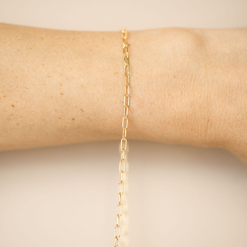 Gold chain bracelet on a person's wrist against a neutral background