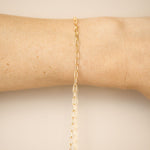 Gold chain bracelet on a person's wrist against a neutral background