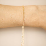 Gold chain bracelet on a person's wrist against a neutral background