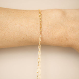 Gold chain bracelet on a person's wrist against a neutral background