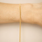 Gold chain bracelet on a wrist against a beige background