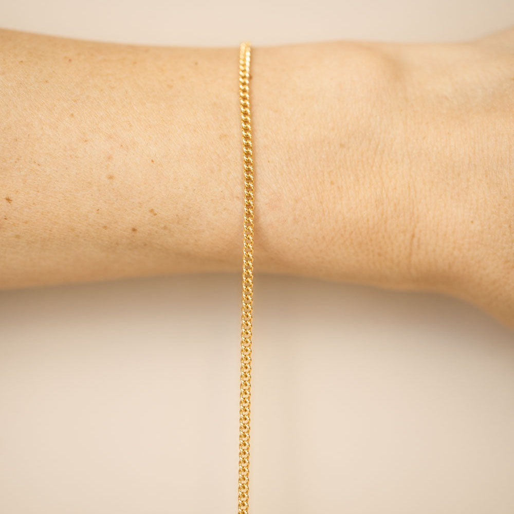 Gold chain bracelet on a wrist against a beige background