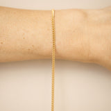 Gold chain bracelet on a wrist against a beige background
